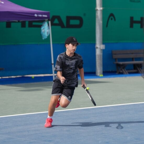 A boy learning tennis on a hard court.