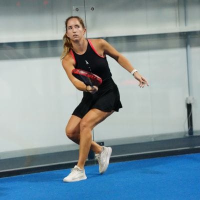 A player mid-point on an indoor blue padel court.