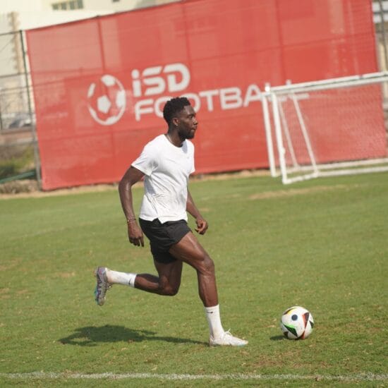 A footballer training on a natural grass pitch beside an ISD Football banner.