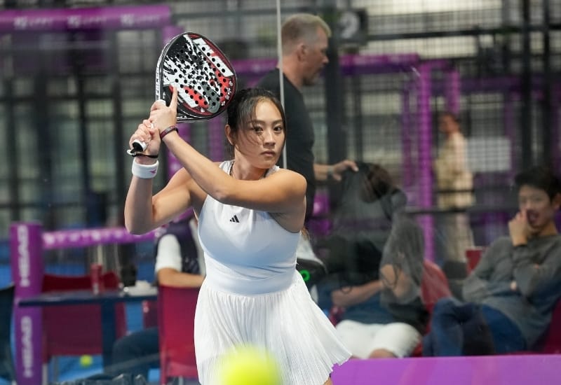 A padel player mid-rally on an outdoor court.